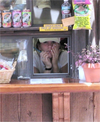 A young girl inside the window of a snack service shack.